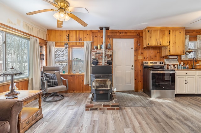 kitchen with hanging light fixtures, a wood stove, light hardwood / wood-style floors, and stainless steel range with electric stovetop