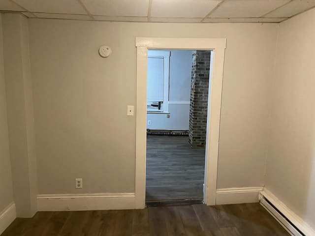 empty room with baseboard heating, a paneled ceiling, and dark wood-type flooring