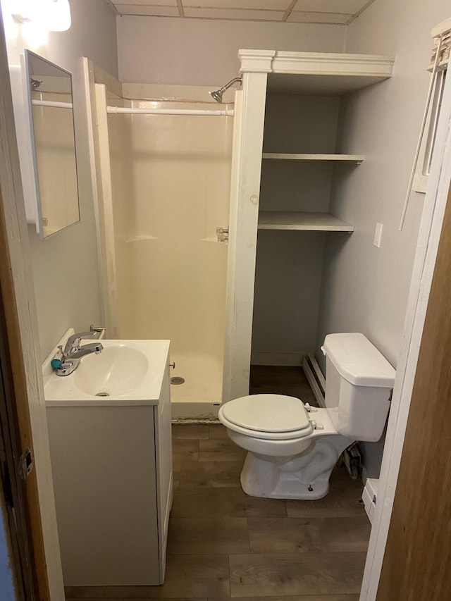 bathroom with a baseboard heating unit, vanity, wood-type flooring, a shower, and toilet