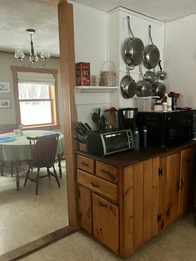 kitchen with a toaster, brown cabinets, dark countertops, a textured ceiling, and a chandelier