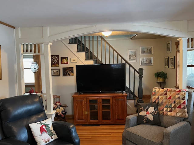 living room with arched walkways, light wood-style flooring, stairway, and decorative columns