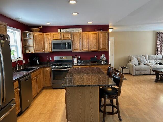 kitchen with sink, appliances with stainless steel finishes, a kitchen island, a kitchen bar, and light wood-type flooring