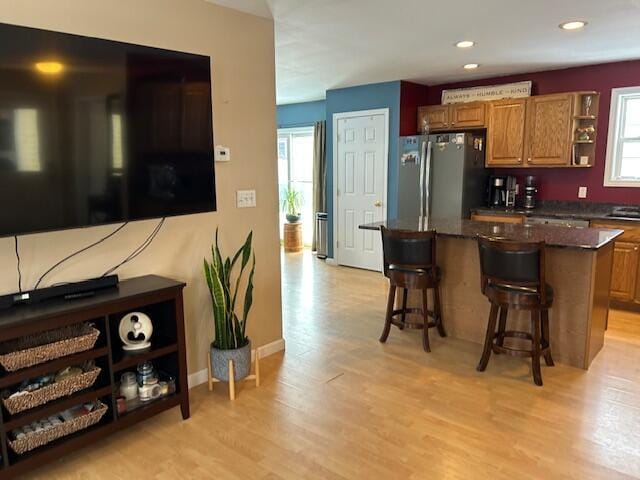 kitchen with stainless steel refrigerator, dark stone countertops, a kitchen breakfast bar, a center island, and light hardwood / wood-style floors