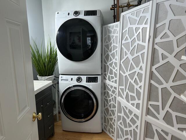 washroom featuring cabinets, stacked washing maching and dryer, and hardwood / wood-style floors