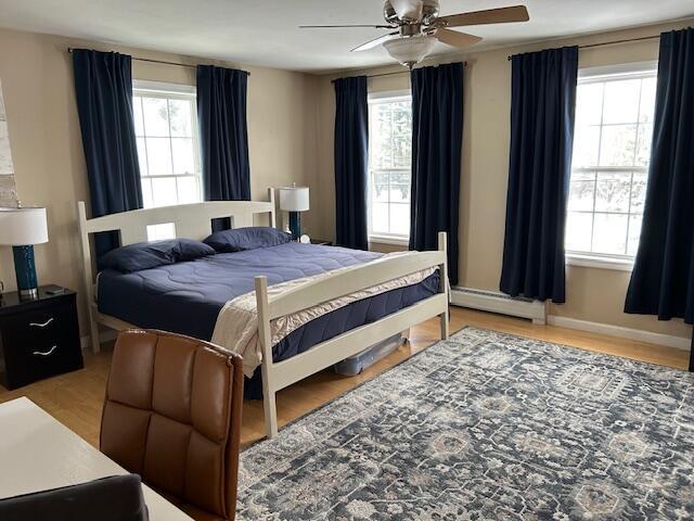 bedroom with multiple windows, a baseboard heating unit, hardwood / wood-style floors, and ceiling fan