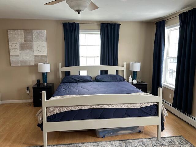 bedroom featuring ceiling fan, a baseboard heating unit, and light hardwood / wood-style floors