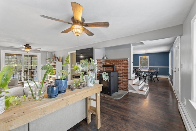 interior space with a baseboard heating unit, a wood stove, dark wood-type flooring, and ceiling fan