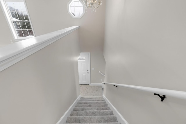 staircase with an inviting chandelier and carpet