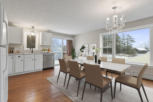 dining space with wood-type flooring, sink, a notable chandelier, and baseboard heating