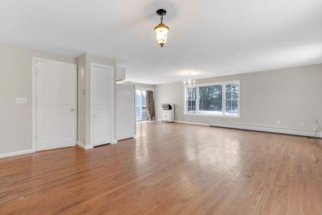 unfurnished living room featuring a baseboard radiator, wood-type flooring, and a notable chandelier