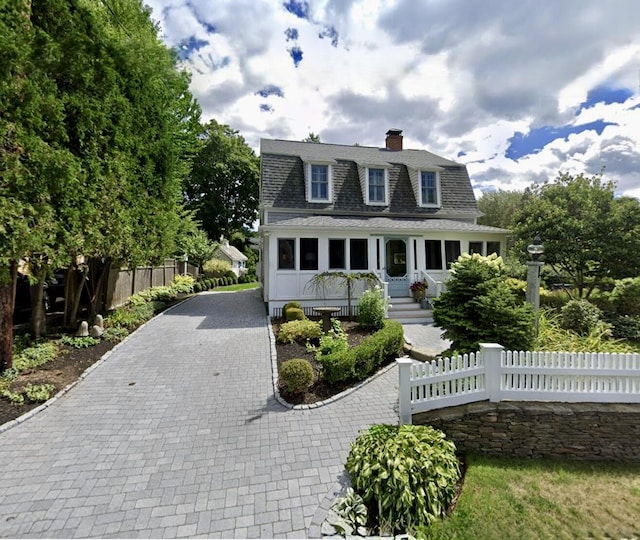 dutch colonial featuring roof with shingles, decorative driveway, a fenced front yard, and a chimney