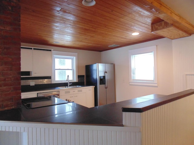 kitchen featuring dark countertops, appliances with stainless steel finishes, a sink, wooden ceiling, and a peninsula