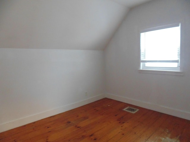 additional living space featuring light wood-style flooring, visible vents, vaulted ceiling, and baseboards