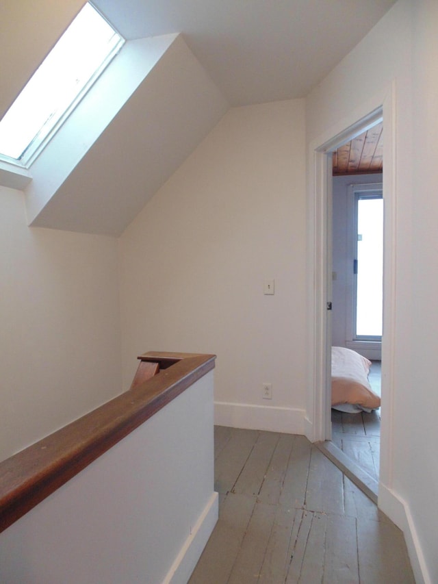 hallway with vaulted ceiling with skylight, an upstairs landing, and baseboards