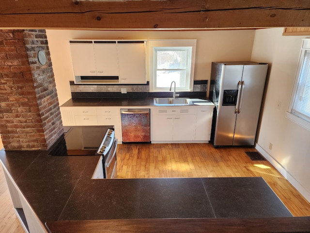 kitchen with light wood-style flooring, stainless steel appliances, a sink, visible vents, and dark countertops