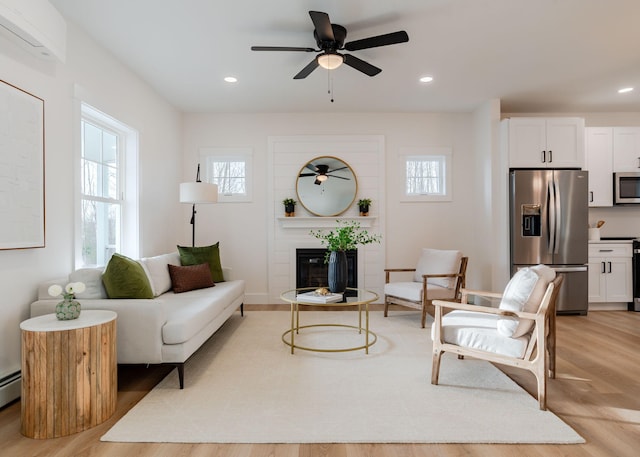 living room featuring a tiled fireplace, light hardwood / wood-style flooring, and ceiling fan