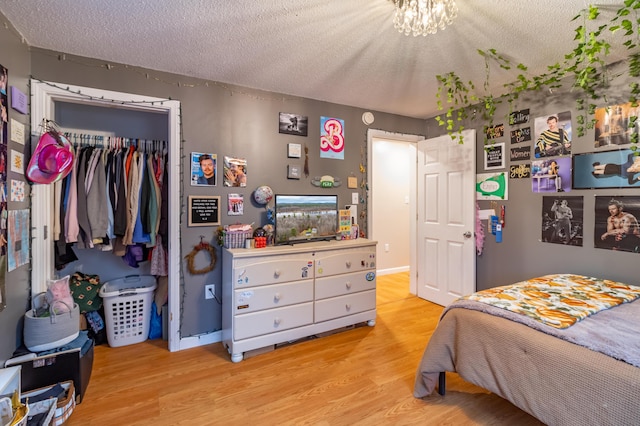 bedroom featuring a closet, a chandelier, a textured ceiling, and light wood-type flooring