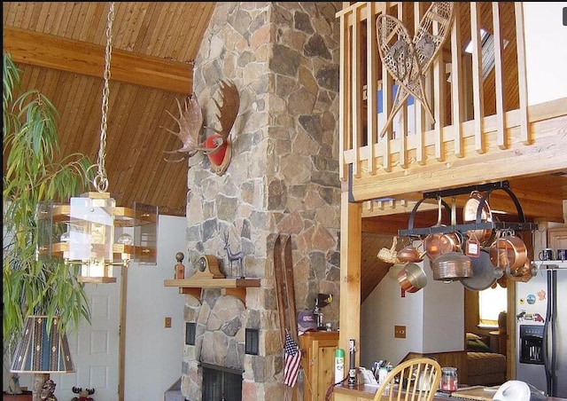 interior space with a stone fireplace, a high ceiling, stainless steel refrigerator with ice dispenser, wooden ceiling, and beam ceiling