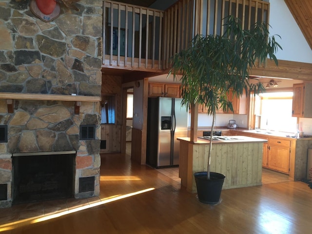 kitchen with stainless steel appliances, a stone fireplace, a high ceiling, and light wood-type flooring