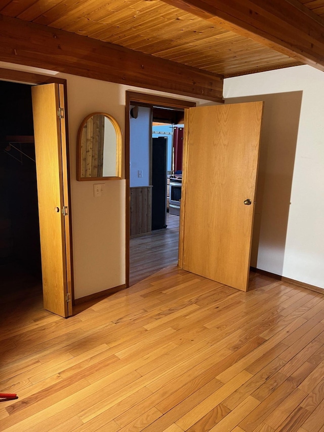 empty room featuring beamed ceiling, wooden ceiling, and light wood-type flooring