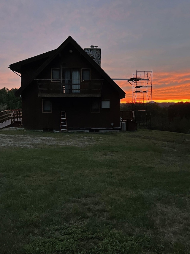 back house at dusk featuring a lawn, a balcony, and central air condition unit