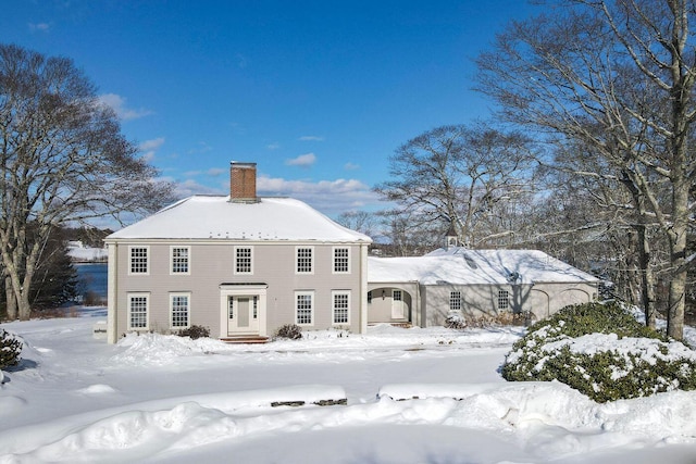 snow covered rear of property with a chimney