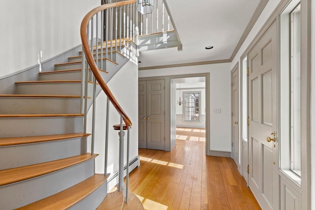 entrance foyer with light wood finished floors, a baseboard radiator, stairway, and ornamental molding