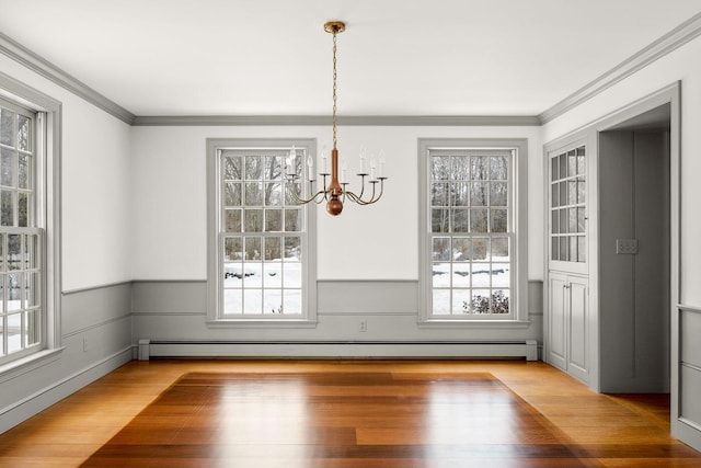 unfurnished dining area featuring an inviting chandelier, a baseboard radiator, crown molding, and wood finished floors