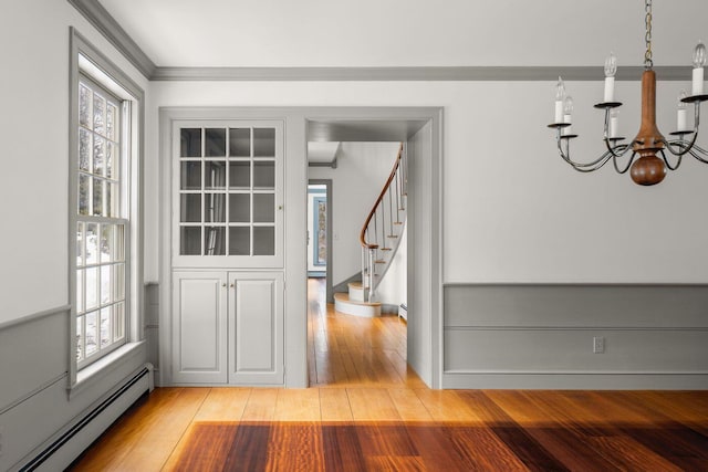 unfurnished dining area featuring stairway, baseboard heating, light wood-style floors, ornamental molding, and a chandelier