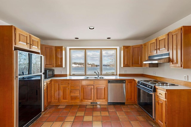 kitchen with brown cabinets, under cabinet range hood, light countertops, black appliances, and a sink