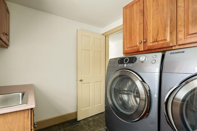 clothes washing area featuring dark tile patterned floors, a sink, baseboards, washer and dryer, and cabinet space