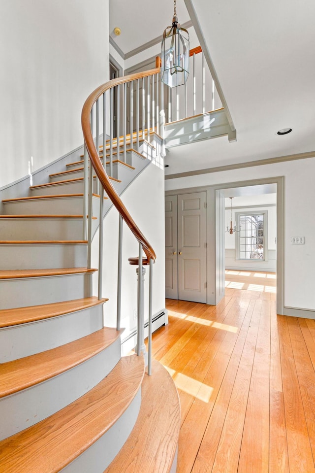 stairs featuring hardwood / wood-style floors, a high ceiling, baseboard heating, and a notable chandelier