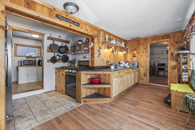 kitchen with light wood-type flooring, wooden walls, and appliances with stainless steel finishes