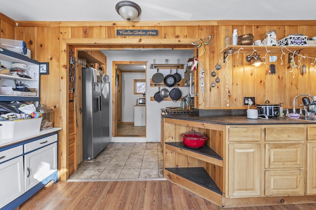 kitchen featuring stainless steel fridge with ice dispenser, light hardwood / wood-style flooring, sink, and wood walls