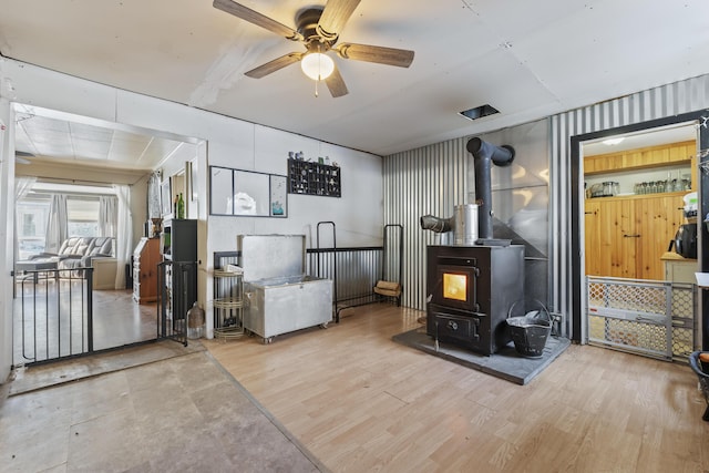 interior space with light wood-type flooring, ceiling fan, and a wood stove