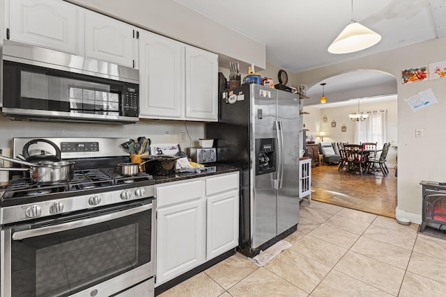 kitchen featuring arched walkways, stainless steel appliances, white cabinets, hanging light fixtures, and dark countertops