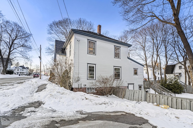 snow covered rear of property with stairs and a chimney