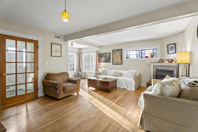 living room featuring light wood-style floors, a tile fireplace, beam ceiling, and visible vents