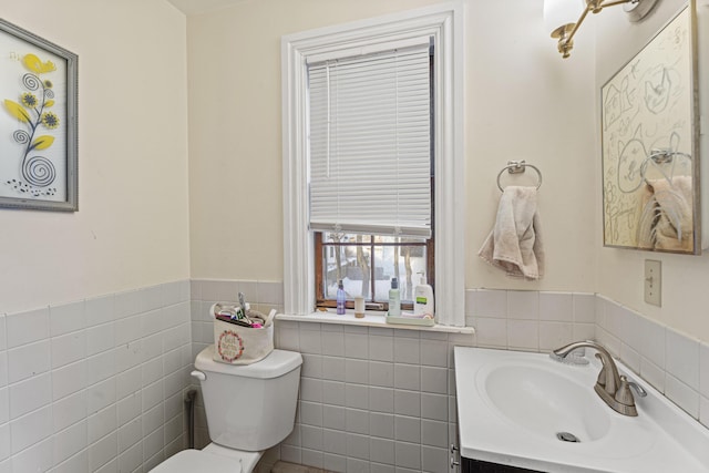 half bathroom with toilet, a wainscoted wall, tile walls, and vanity