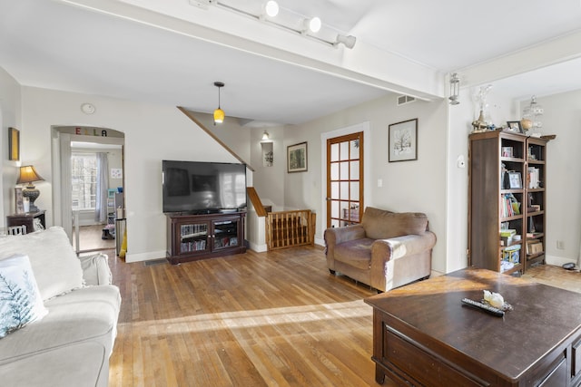 living area featuring baseboards, visible vents, wood finished floors, and beamed ceiling