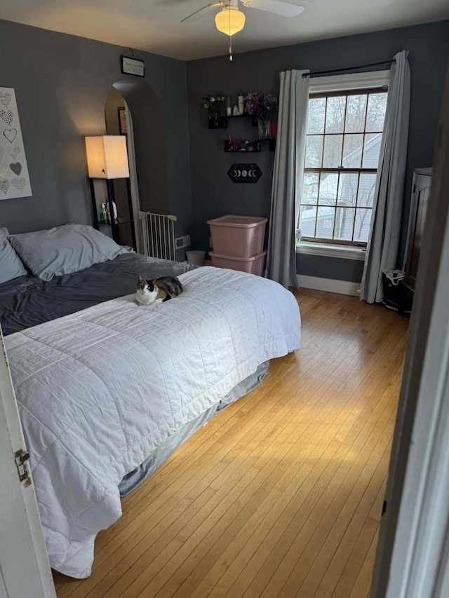 bedroom with arched walkways, wood finished floors, a ceiling fan, and baseboards