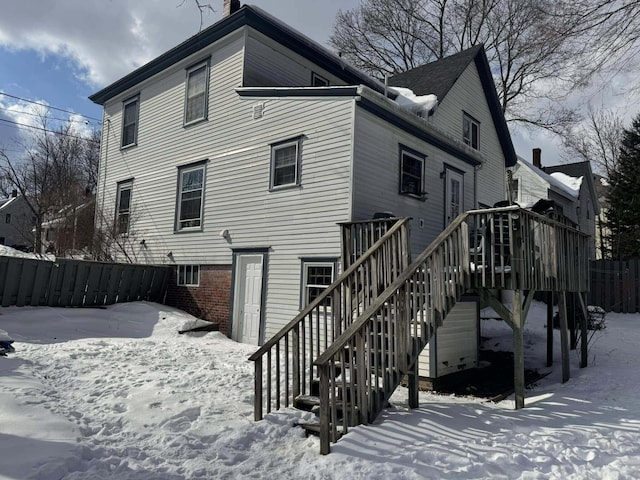 snow covered rear of property with stairway and brick siding