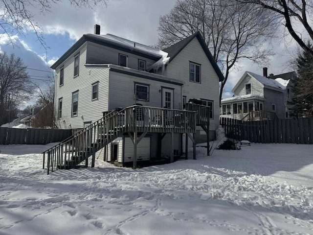 snow covered rear of property with a deck, fence, and stairway