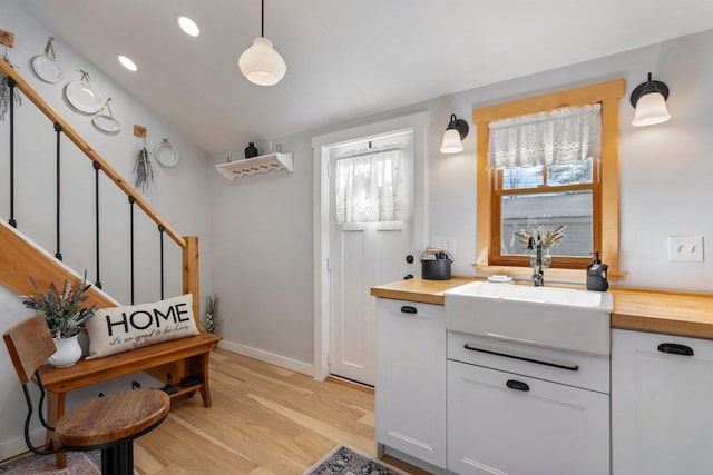 kitchen with sink, light wood-type flooring, decorative light fixtures, butcher block countertops, and white cabinets