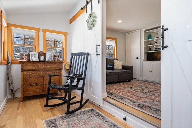 living area with a barn door, light wood-type flooring, and vaulted ceiling