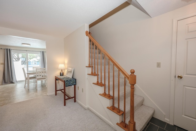 stairway featuring a textured ceiling, carpet floors, and baseboards