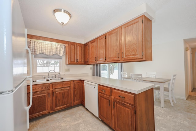 kitchen with white appliances, brown cabinetry, a peninsula, light countertops, and a sink