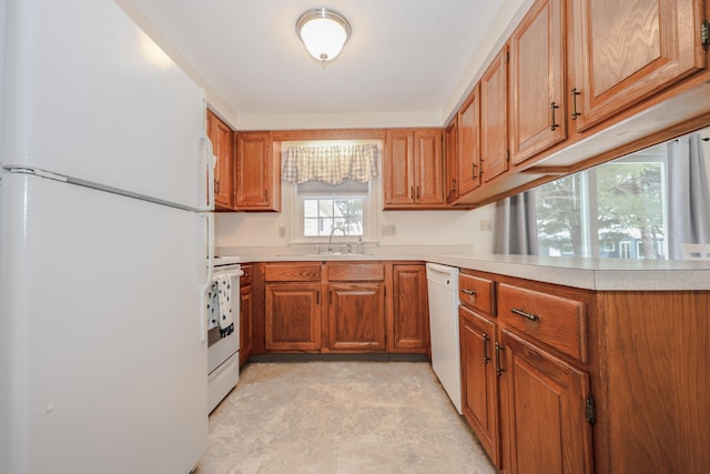 kitchen featuring brown cabinetry, white appliances, light countertops, and a sink