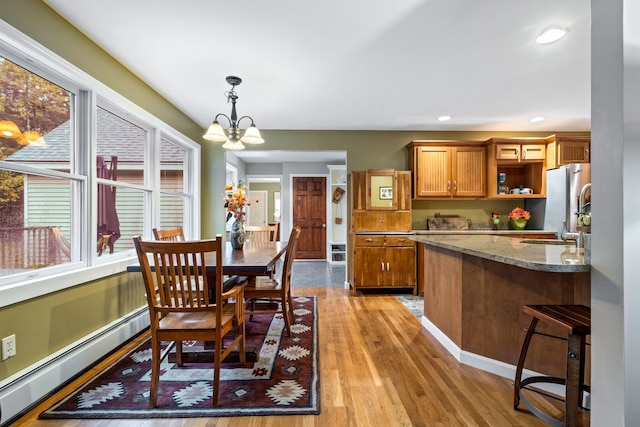 dining area featuring an inviting chandelier, sink, a baseboard radiator, and light wood-type flooring