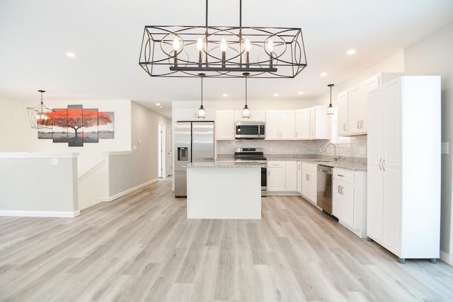 kitchen with a kitchen island, appliances with stainless steel finishes, white cabinetry, sink, and light stone countertops